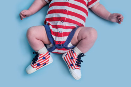 A newborn baby dressed in the colors of the American flag of the United States, blue studio background. A child in the clo...