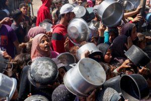 Palestinians wait to receive food cooked by a charity kitchen, in Khan Younis