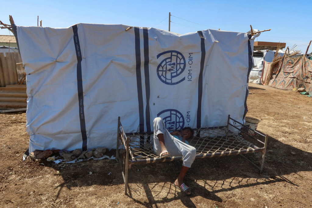 A boy displaced from Gezira state due to Rapid Support Forces (RSF) violence, lies down on a bench with the logo of the In...