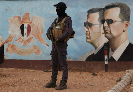 A member of the former rebel group Hayat Tahrir al-Sham stands guard near an image of Syria's Bashar al-Assad at the fourt...