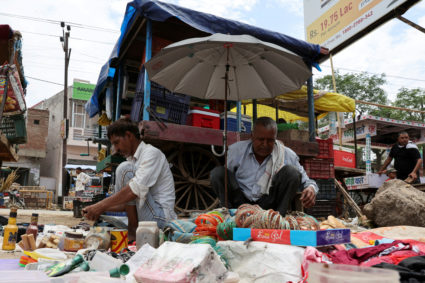 Vendors sit under an umbrella to protect themselves from heat at a local market, in Mathura