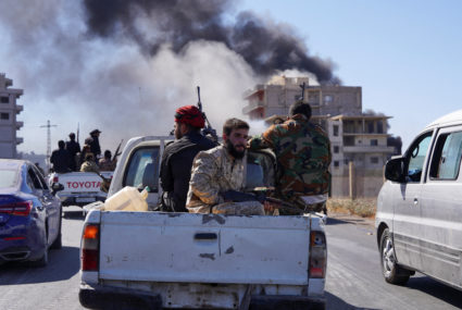Smoke rises while Syrian security forces sit in the back of a truck, in Sweida