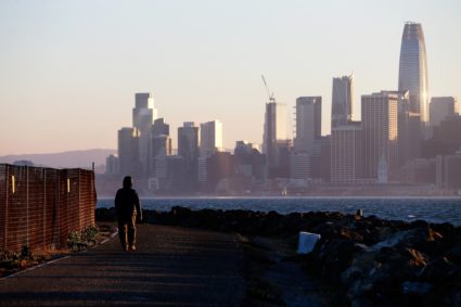 The San Francisco skyline is seen behind a woman as she walks past a condemned area on Treasure Island, near San Francisco