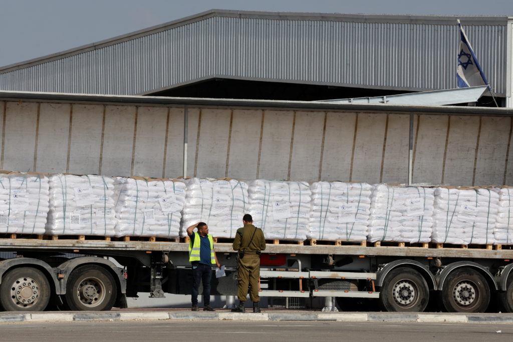 An Israeli security forces member speaks to a worker next to a truck carrying aid at the Kerem Shalom crossing between Isr...