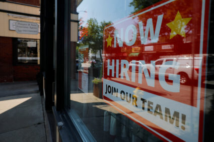 A "Now Hiring" sign hangs in the window of a hair salon in Medford, Massachusetts