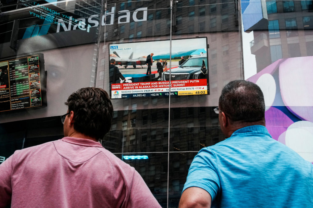 People watch a screen showing U.S. President Donald Trump meeting with Russian President Vladimir Putin in Alaska, at the ...