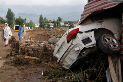 A woman walks past a damaged vehicle following heavy rain and floods in Buner district