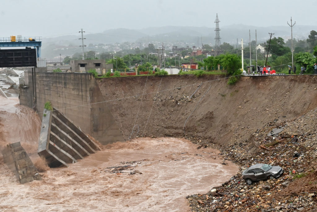 A damaged car lies in the rubble after a part of a bridge collapsed along the Tawi River following heavy rainfall in Jammu