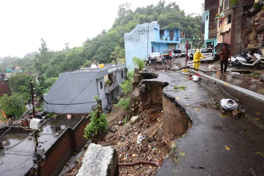 People stand on a damaged road following heavy rain in Jammu