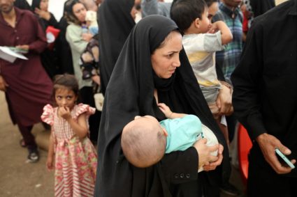 An Afghan woman deported from Iran, holds her child as she waits to register herself at a camp for returning migrants near...