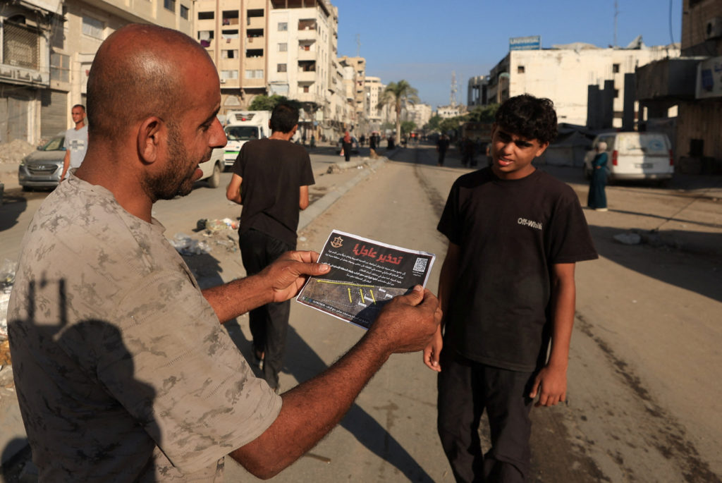 A Palestinian man holds a leaflet, dropped by Israeli forces, ordering residents of Gaza City to evacuate, in Gaza City