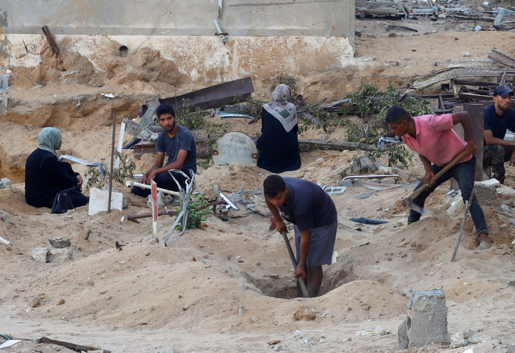 Palestinians bury loved ones killed in Israeli fire, according to medics, in Al-Shifa hospital yard, in Gaza City