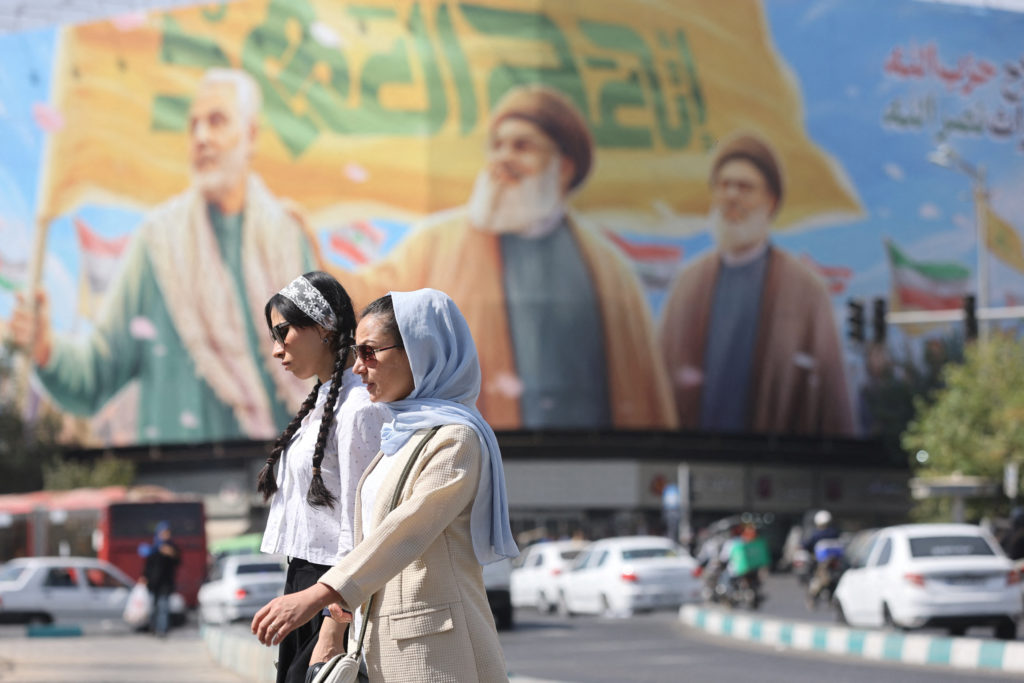 People walk past a billboard with a picture of late Hezbollah leaders Hassan Nasrallah and Hashem Safieddine and senior Ir...