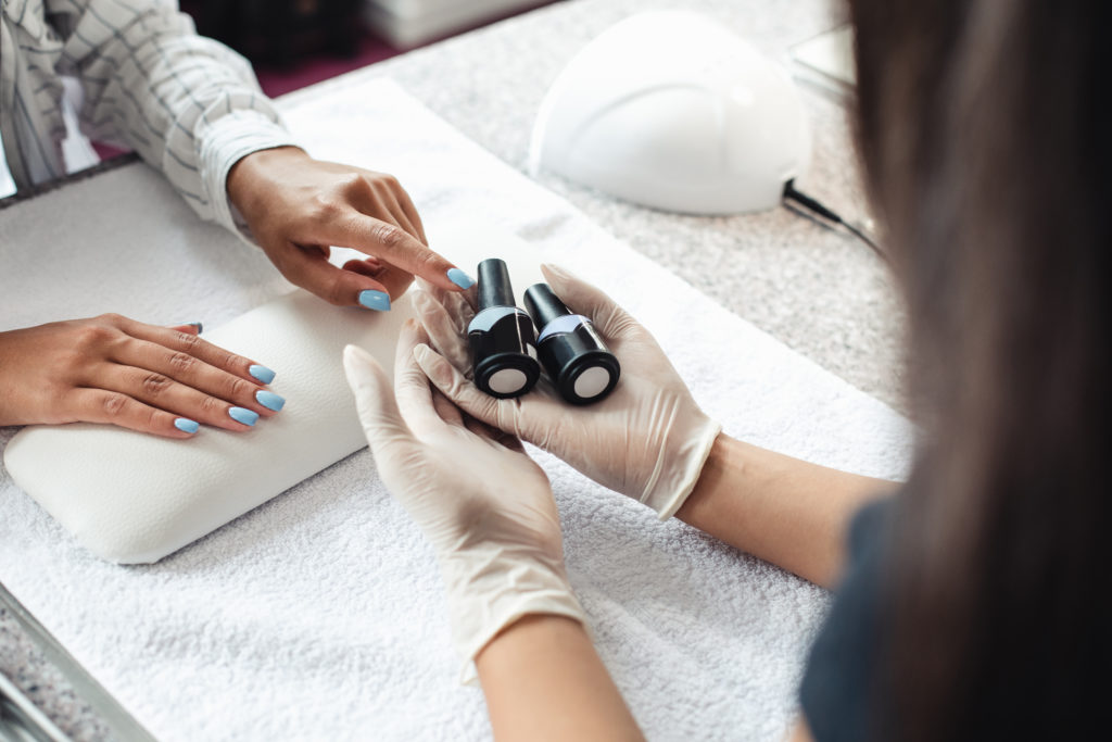 Professional nail care. African american woman client chooses gel polish in hands of master in rubber gloves in modern sal...