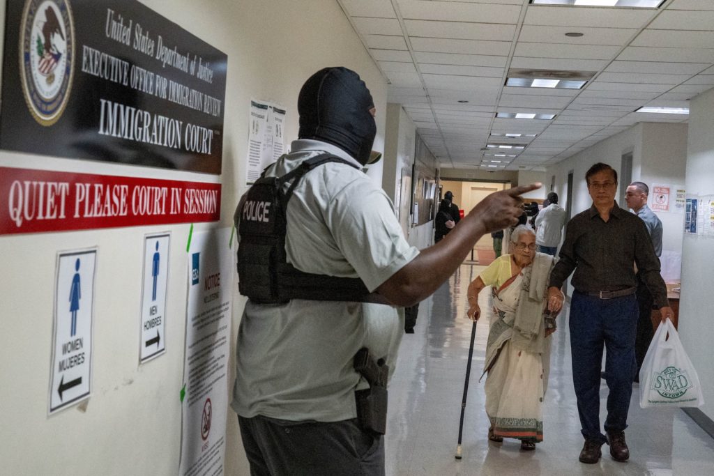 Federal immigration officers wait to carry out detentions as migrants traverse the hallway at U.S. immigration court in Ma...
