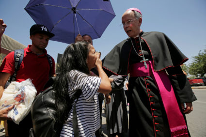 El Paso Bishop Mark Seitz talks with Honduran migrant Cesia as he walks beside her parents at Paso del Norte international...