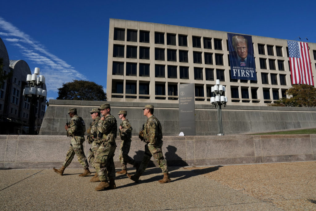 Members of the National Guard walk past a building displaying a banner with an image of U.S. President Donald Trump, in Wa...
