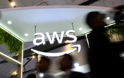 FILE PHOTO: People walk past the logo of Amazon Web Services (AWS) at its exhibitor stall at the India Mobile Congress 202...