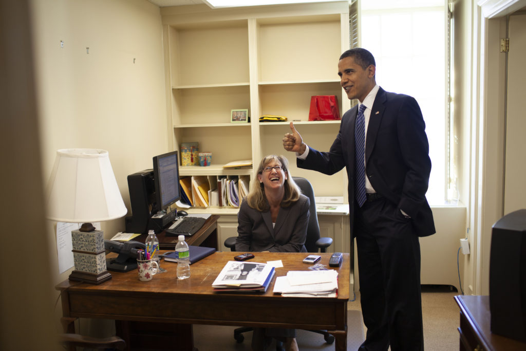 An image of President Barack Obama standing with a White House staffer sitting at her desk.