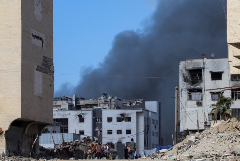Palestinians walk as smoke rises following an Israeli strike, in Gaza City