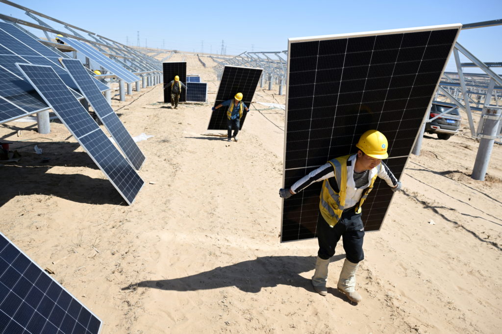 Workers carry solar panels to install them at a solar farm in Lingwu