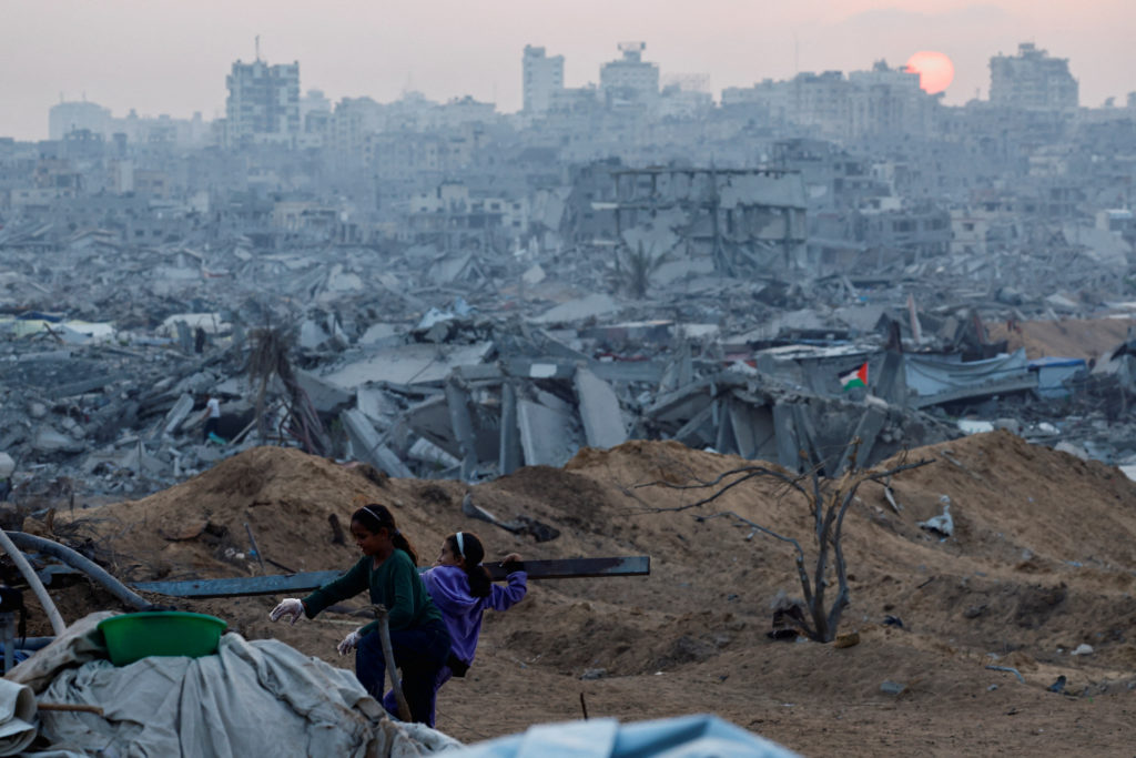 A Palestinian child holds a piece of wood with the rubble of destroyed buildings in the background, amid a ceasefire betwe...