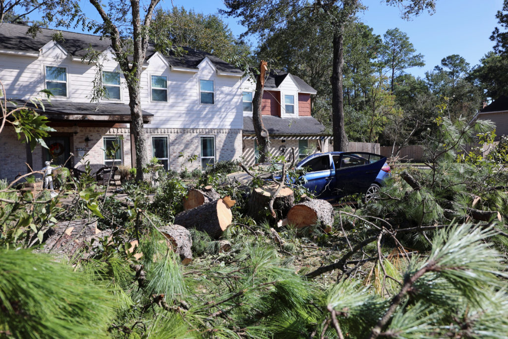 A damaged car and downed trees in front of a home in Spring
