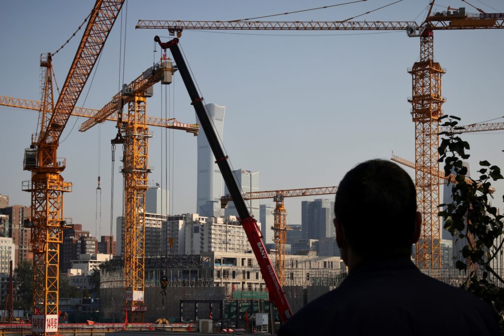A person looks towards cranes in front of the skyline of the Central Business District (CBD) in Beijing