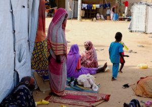 A woman from El Fasher prays surrounded by displaced women, in a camp in Al-Dabbah
