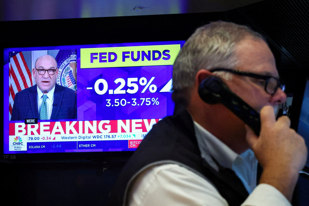 A screen displays the Fed rate announcement as traders work on the floor of the NYSE in New York