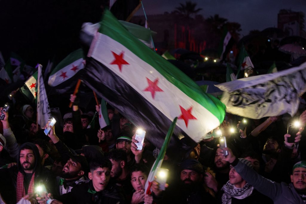 Syrians holds flags as they gather to mark the first anniversary of Bashar al-Assad's fall, in Latakia