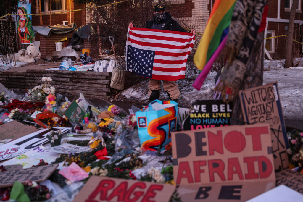 A person holds an upside down U.S. flag while standing by a makeshift memorial at the scene of the fatal shooting of Renee...
