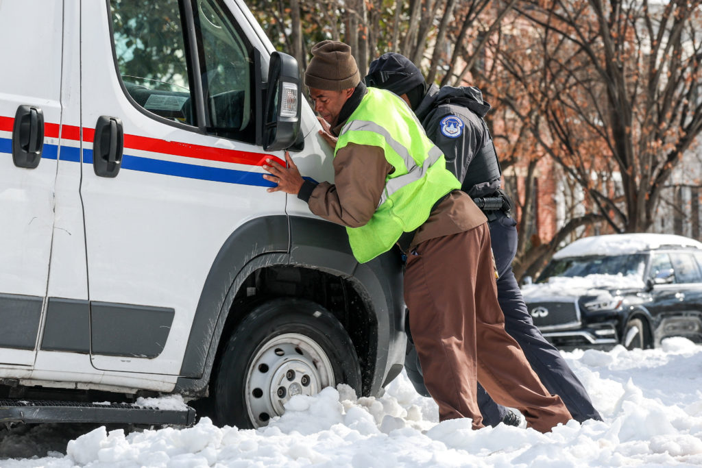 People help push a USPS truck out of snow and ice, two days after a winter storm in Washington