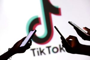FILE PHOTO: Illustration shows teenagers pose for a photo while holding smartphones in front of a TikTok logo