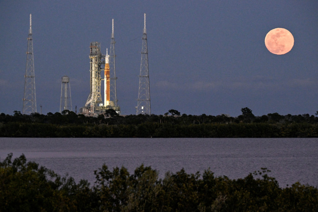 A full moon rises near the Space Launch System (SLS), with the Orion crew capsule, at launch complex 39B