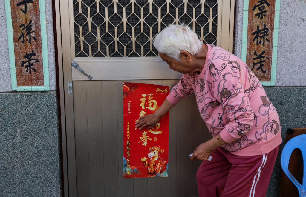 A woman sticks a poster with Spring Festival couplets to a door on the Lunar New Year's Eve, in Donggang
