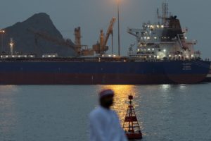 A man sits on the waterfront as vessel sits at anchor inside Sultan Qaboos Port in Muscat