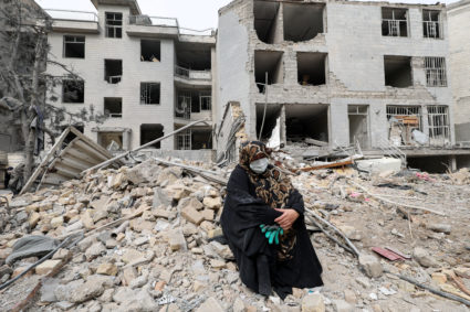 A woman sits outside her destroyed apartment after it was damaged, in Tehran