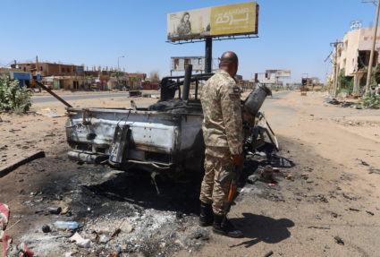 A Sudanese army soldier next to a destroyed combat vehicle in the state of Khartoum