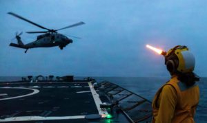 A U.S. sailor signals to an MH-60S Sea Hawk helicopter