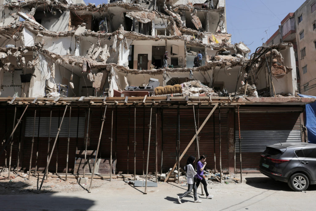 People walk in front of a damaged building in the southern suburbs of Beirut