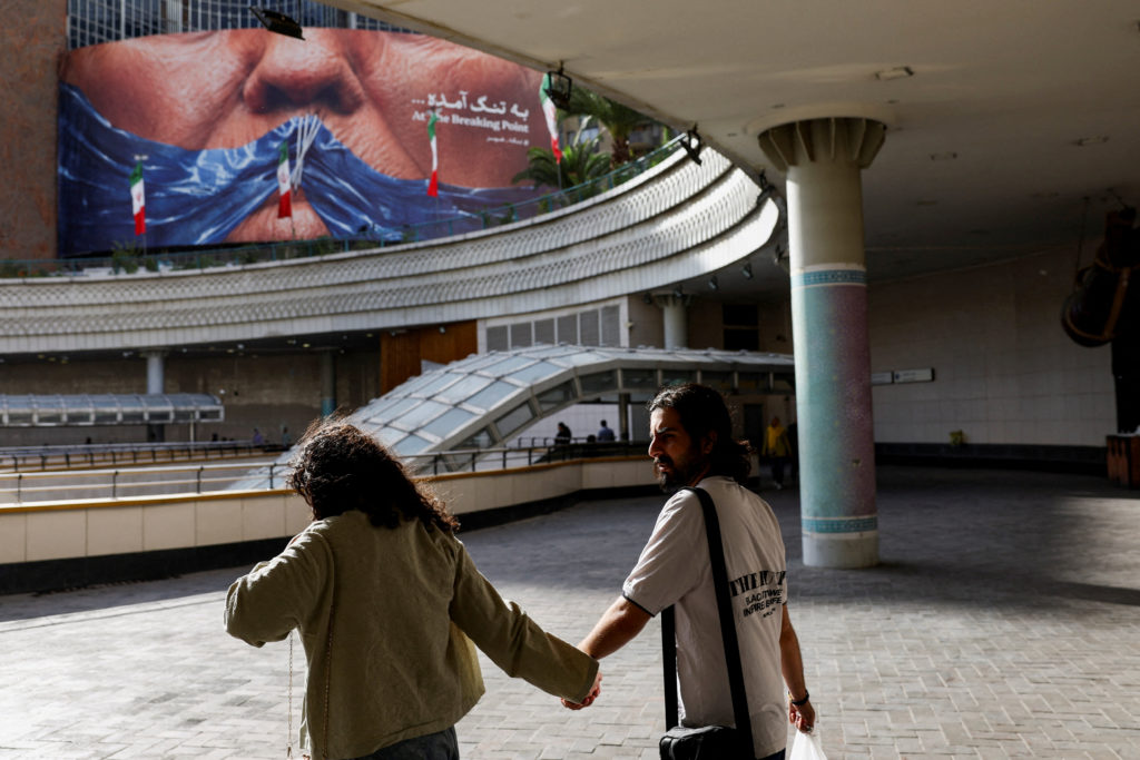 FILE PHOTO: People walk past an anti-U.S. billboard depicting U.S. President Donald Trump and the Strait of Hormuz, in Tehran