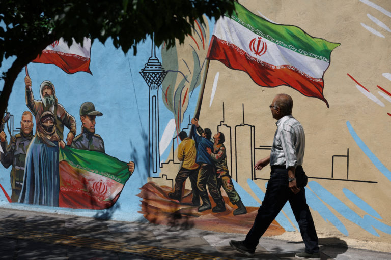 An Iranian man walks next to a mural on a street in Tehran