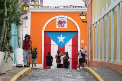 People line up and take photos in front of a mural of the Puerto Rican flag in Old San Juan