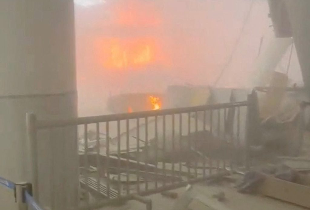 Debris lies on the floor as fire burns in the background in the aftermath of Iranian strikes at Kuwait International Airpo...