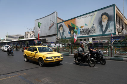 People ride past a mural depicting the late leader of the Islamic Revolution, Ayatollah Ruhollah Khomeini, and the late Ir...