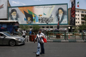 A woman walks near a mural depicting the late leader of the Islamic Revolution, Ayatollah Ruhollah Khomeini, and Iran's la...