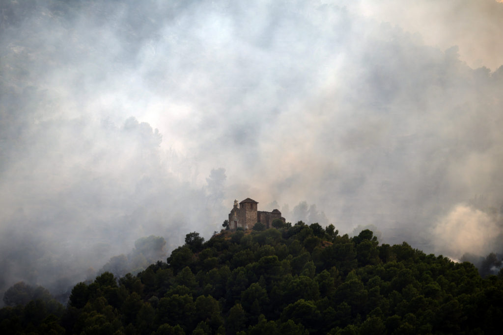 Ermita de Santa Barbara church with smoke on the background from a wildfire in Onda