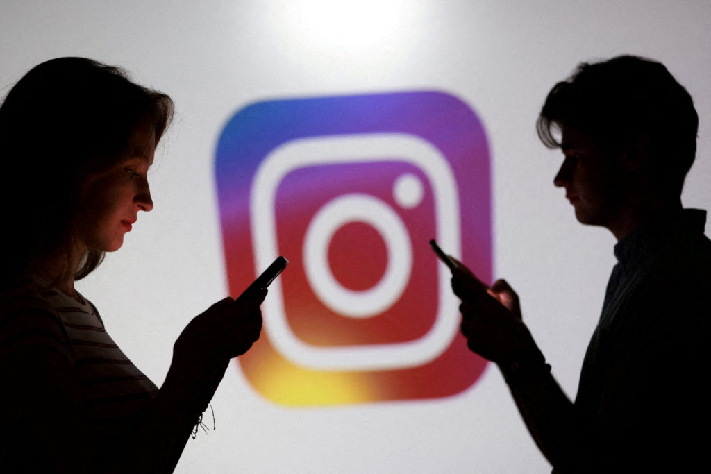 FILE PHOTO: Illustration shows teenagers pose for a photo while holding smartphones in front of an Instagram logo