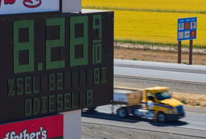 Semis drive past sign showing fuel prices